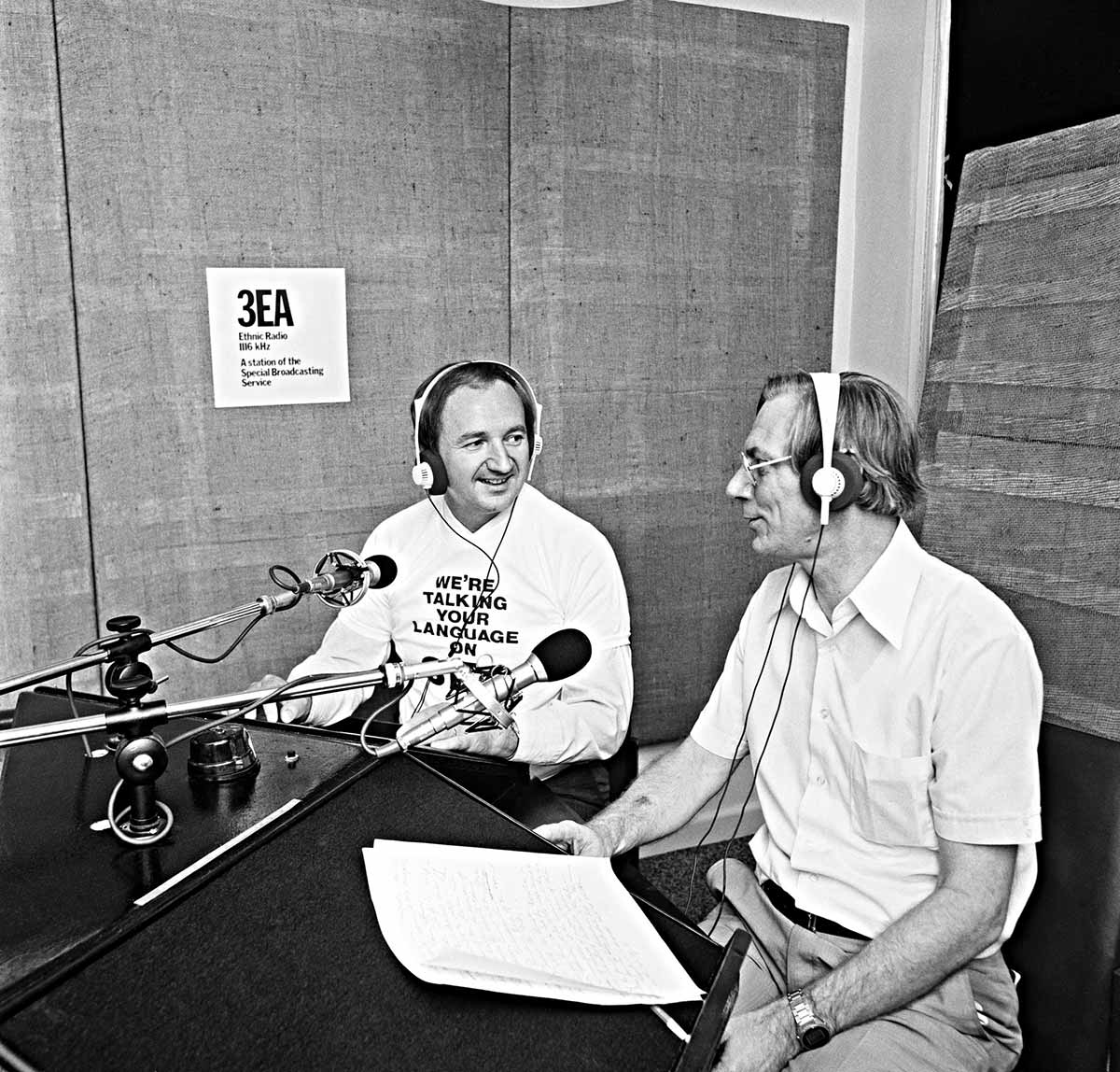 Two men sitting in a radio studio in front of microphones. They are smiling and clearly in conversation. The present is wearing a top saying ‘We’re talking your language on 3EA’.