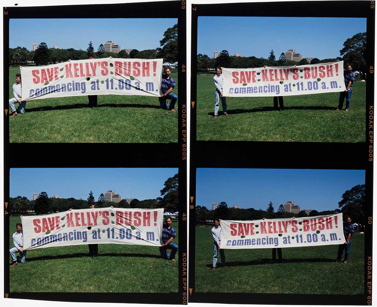 Colour photograph of two men holding up a protest banner that reads 'Save Kelly's Bush! commencing at 11:00am.'
