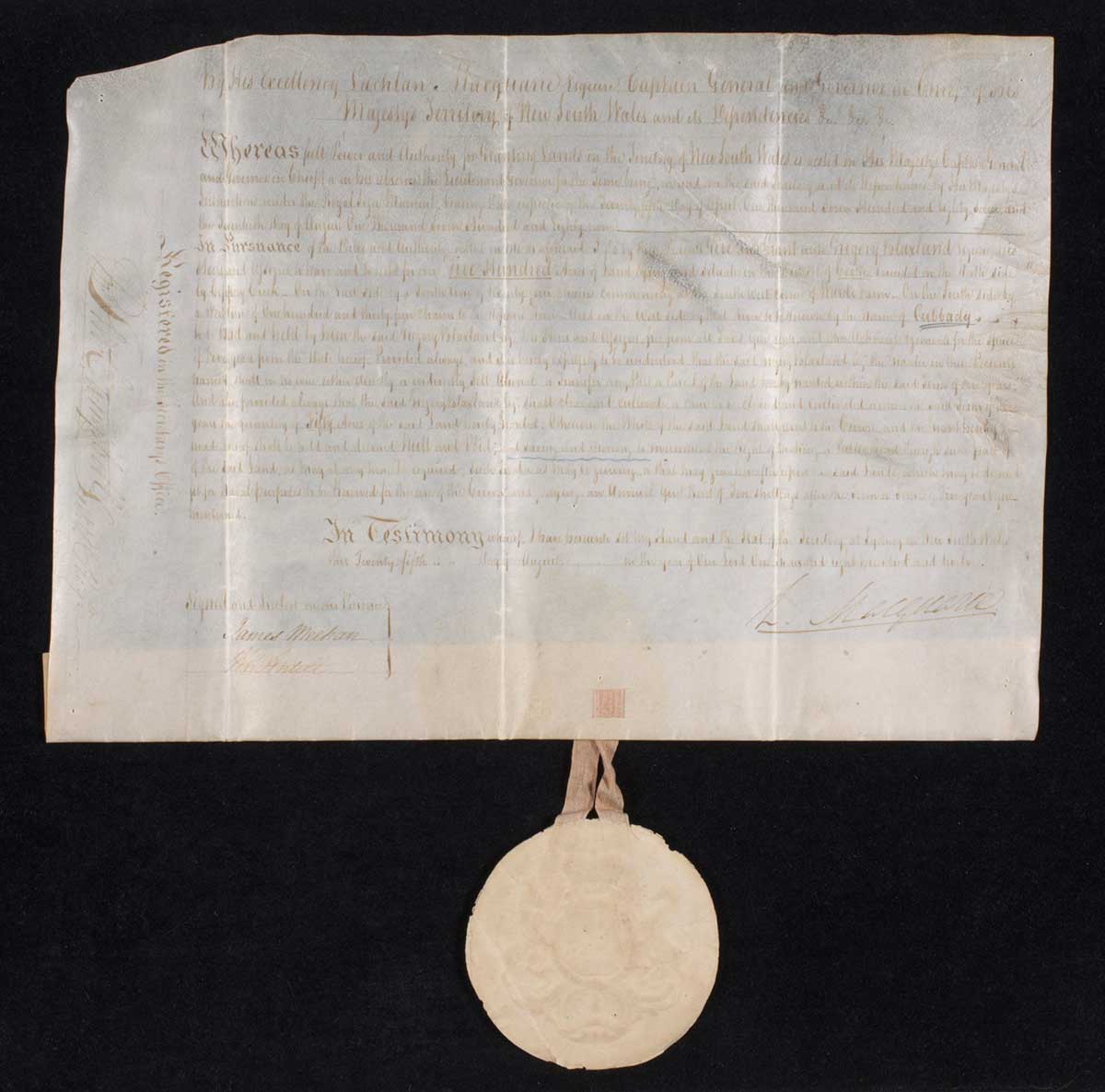 A handwritten white coloured vellum land grant made out to Gregory Blaxland that reads 'By His Exellency Lachlan Macquarie ...'. The document is dated 25th August 1812. The round shaped seal hangs freely from the bottom, attached by a beige coloured ribbon.