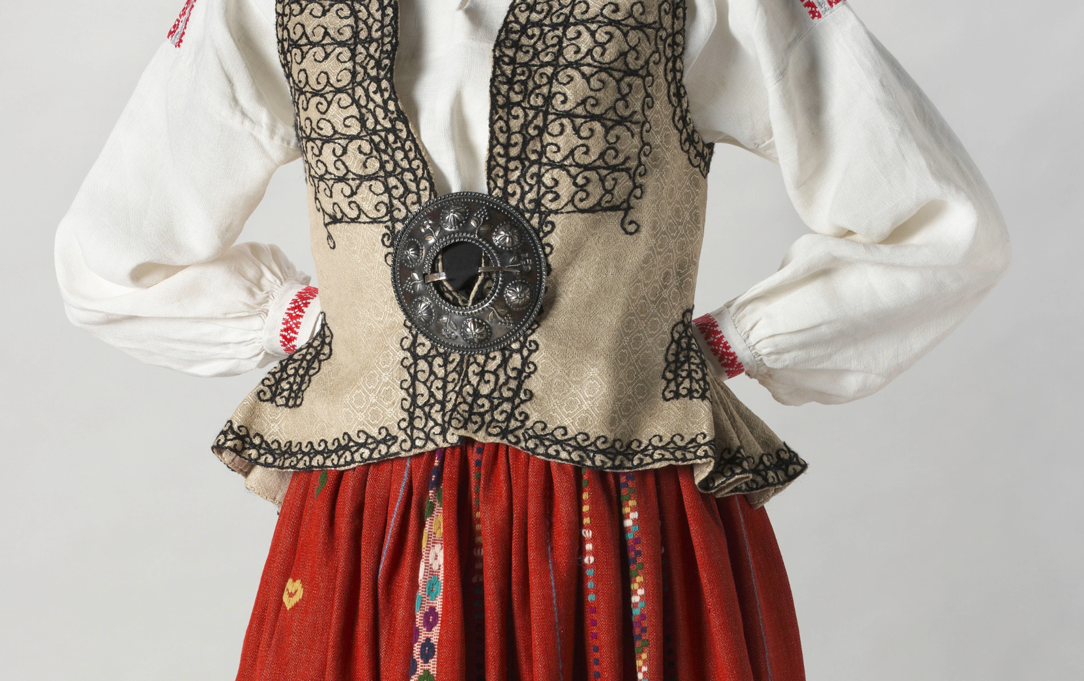 A white linen shift blouse decorated with embroidered geometric patterns in red and grey at the collar, the cuffs and the shoulders.