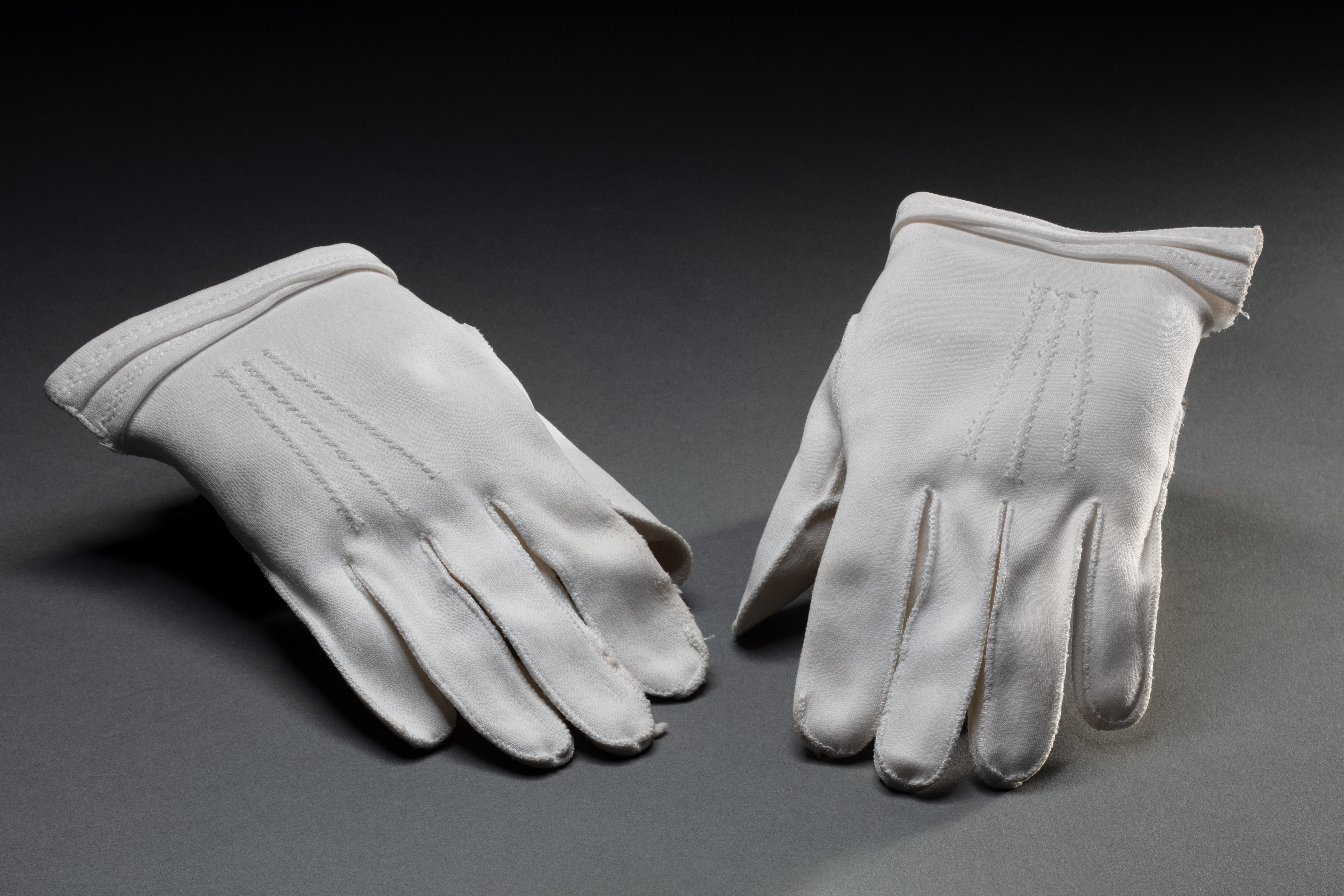  A pair of ladies' short white gloves, without a manufacturer's label. They have a zig zag stitch decoration and partial double fold at hem to wrist edge.