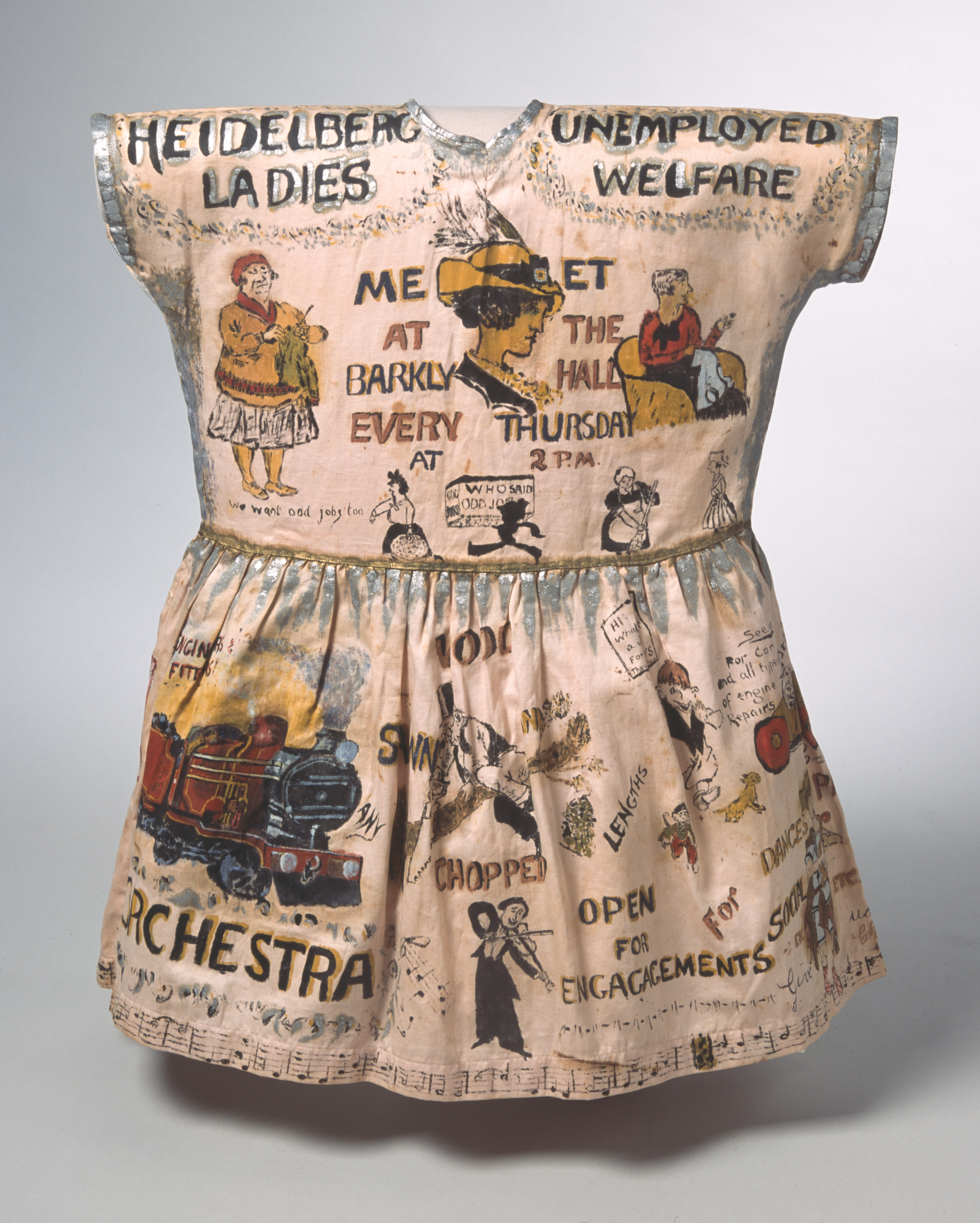 A girl’s fancy dress garment, hand-painted with cartoons and caricatures showing the work of the Heidelberg Unemployment Bureau. The dress is light peach in colour, with ochre yellow, red, black, white and silver coloured paints forming the bulk of the illustrations. Across the shoulders either side of the collar are the words 'HEIDELBERG UNEMPLOYED / LADIES WELFARE'.