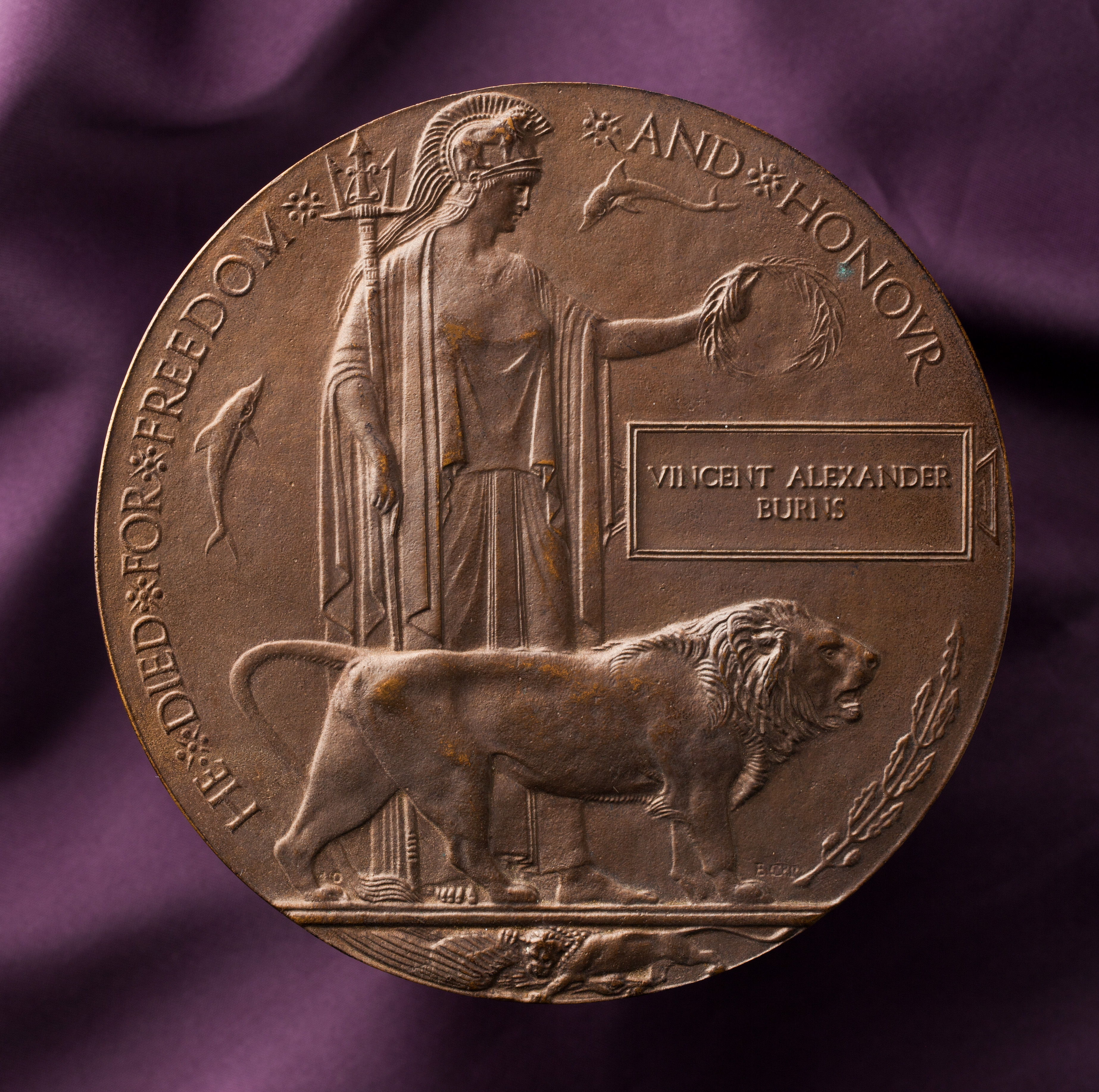  A circular, bronze next-of-kin Plaque (or Memorial Plaque) with a rectanglular tablet and the name 'VINCENT ALEXANDER / BURNS'. The plaque is plain on one side and has a raised design on the other, featuring Britannia holding a trident and standing with a lion at her feet. Her outstretched arm is holding an oak wreath. Two dolphins swim around Britannia and a second lion is depicted at the lower edge tearing apart a German eagle. The text 'HE DIED FOR FREEDOM AND HONOUR' is cast around the picture.