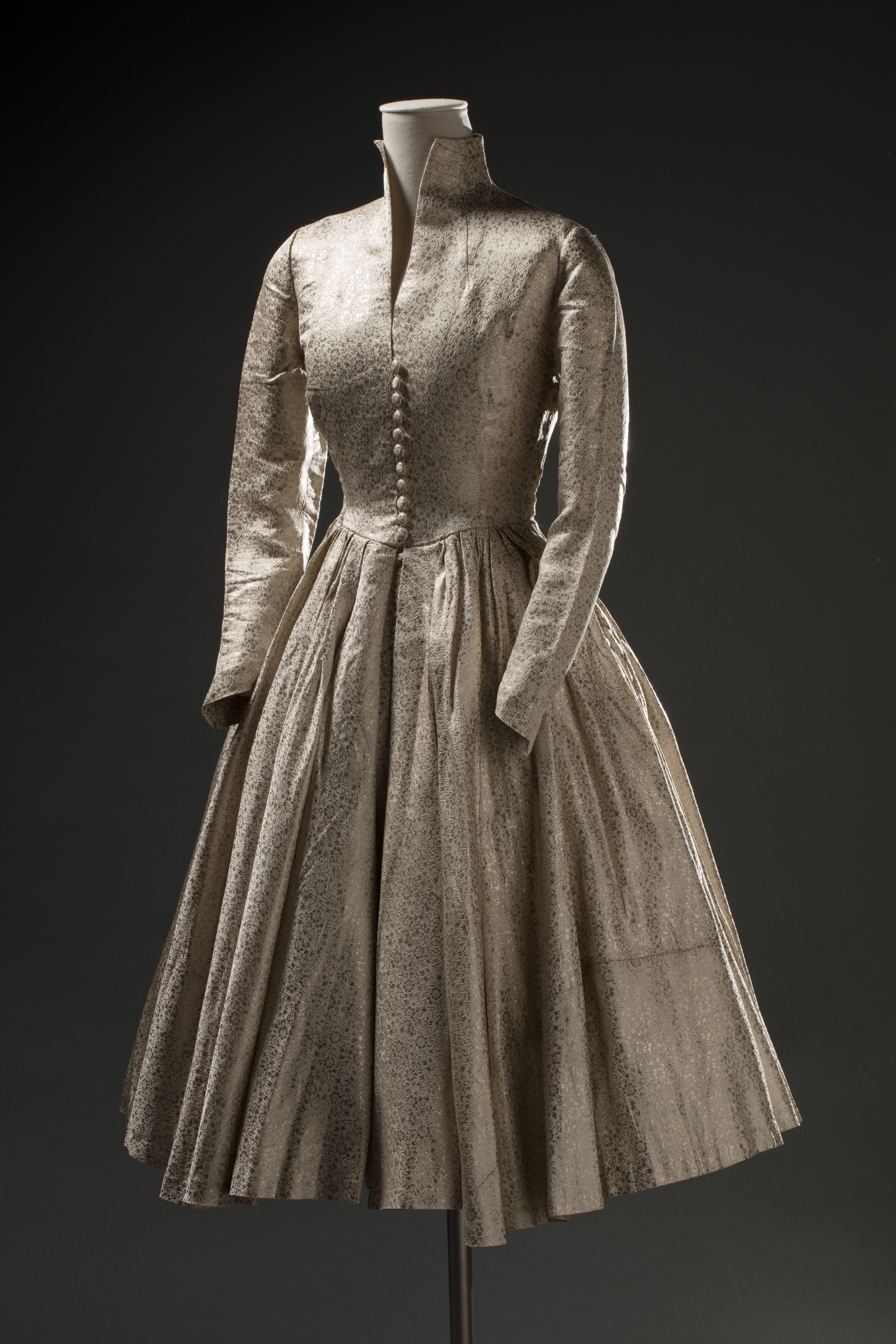  A synthetic brocade wedding dress. The dress is cream coloured with a metallic silver floral detailing. No labels are attached.