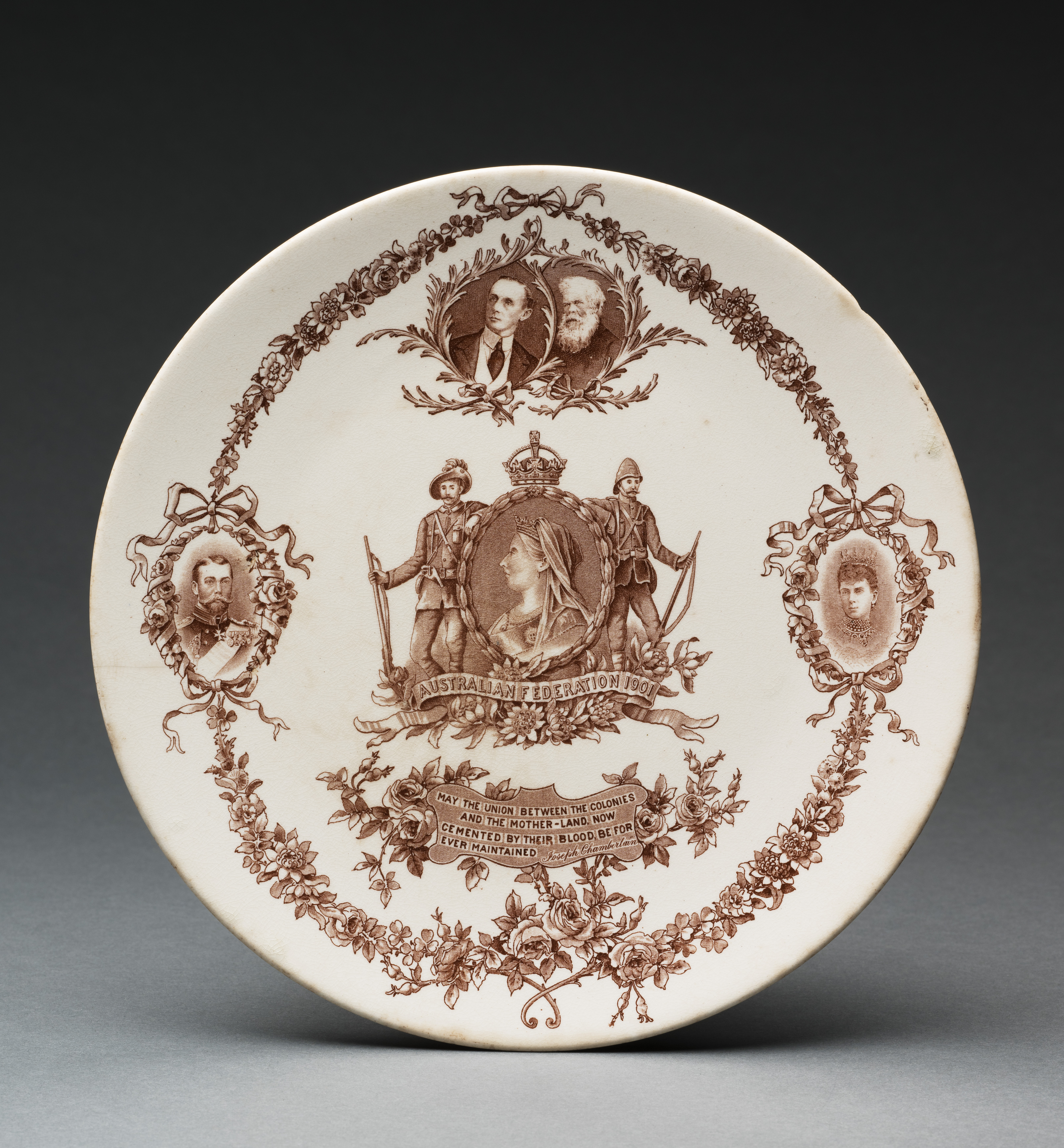  A cream earthenware plaque with a faded gilt rim. Decorated on the front with a sepia transfer print of Queen Victoria centred inside a wreath border flanked by a British and an Australian soldier, and 'AUSTRALIAN FEDERATION 1901' inscribed within a ribbon banner amongst waratahs at the bottom. Inscribed below 'MAY THE UNION BETWEEN THE COLONIES / AND THE MOTHER-LAND NOW / CEMENTED BY THEIR BLOOD BE FOR / EVER MAINTAINED Joseph Chamberlain', and above are portraits of Sir Henry Parkes and Lord Hopetoun.