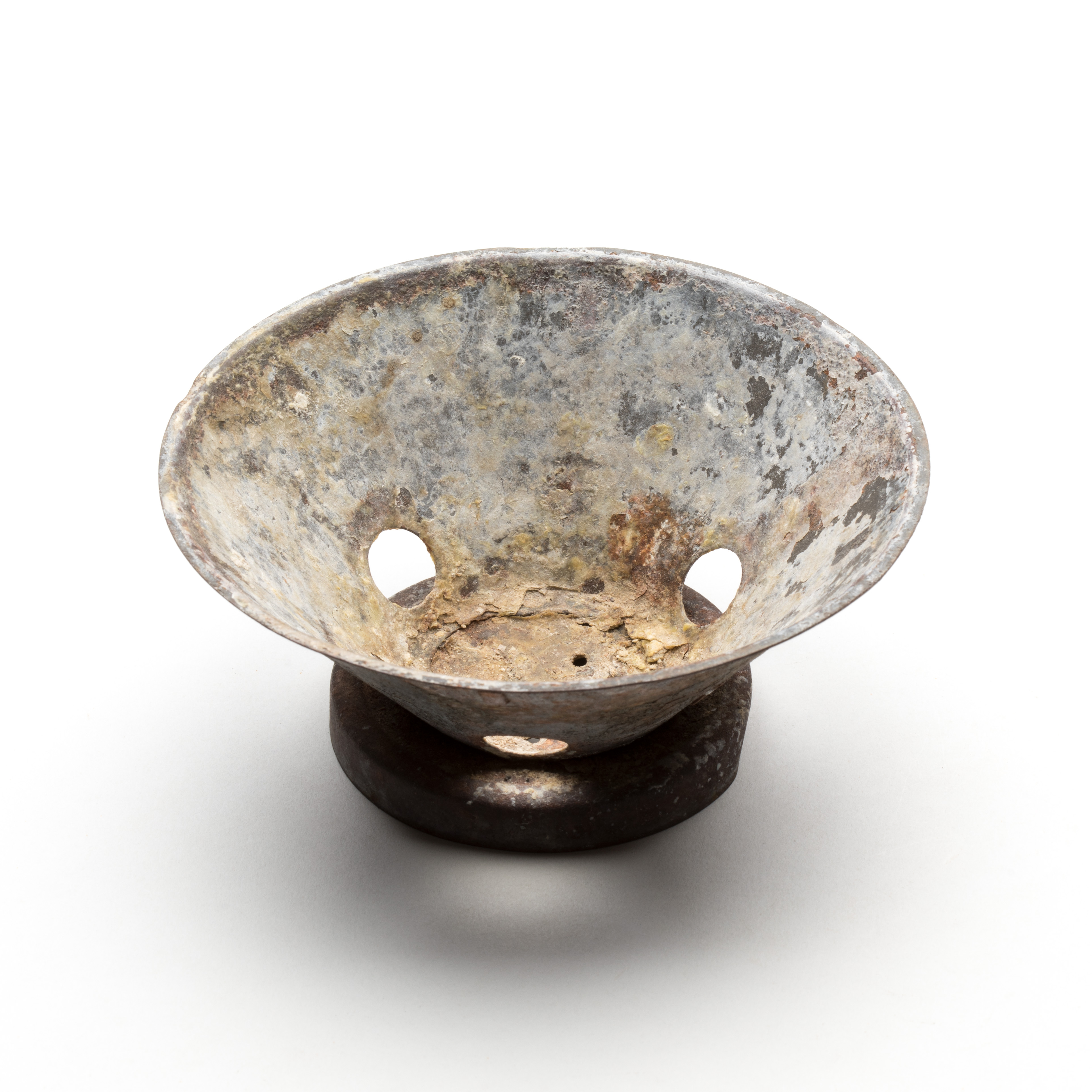 A soap holder improvised from part of an unknown circular tin object and a tin lid. The tin lid has drainage holes punctured into it and is soldered to the bottom of the circular part to form a stand.
