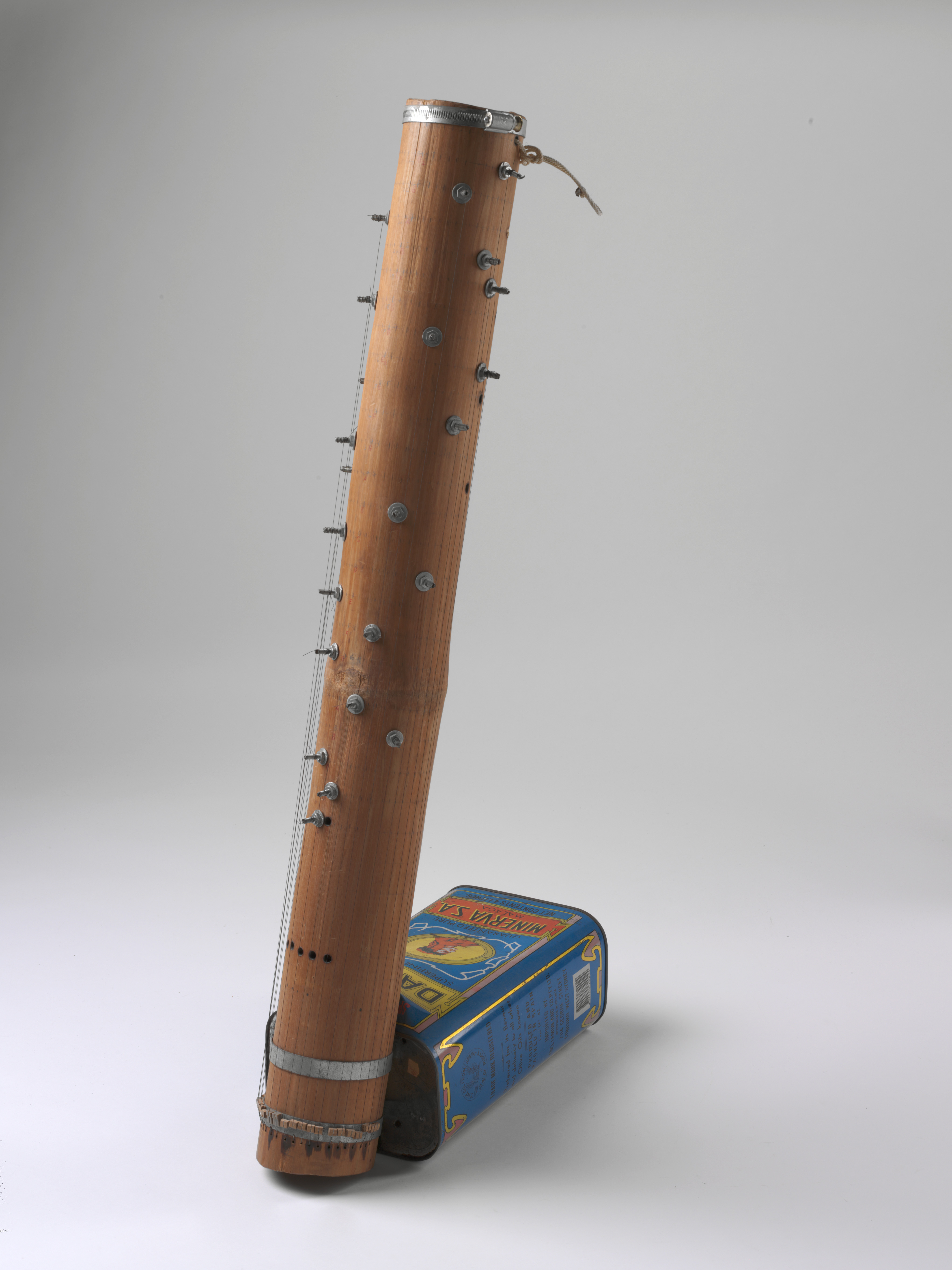  A bamboo hybrid musical instrument called a 'dan tre'. The instrument has twenty-three 800mm-long wire strings attached to a bamboo tube. An Australian-made metal hose-clamp is around the top rim, and an Australian 'DANTE' brand rectangular four-litre olive oil tin, which acts as a resonator, is strapped to the base of the tube with two metal hose clamps. 