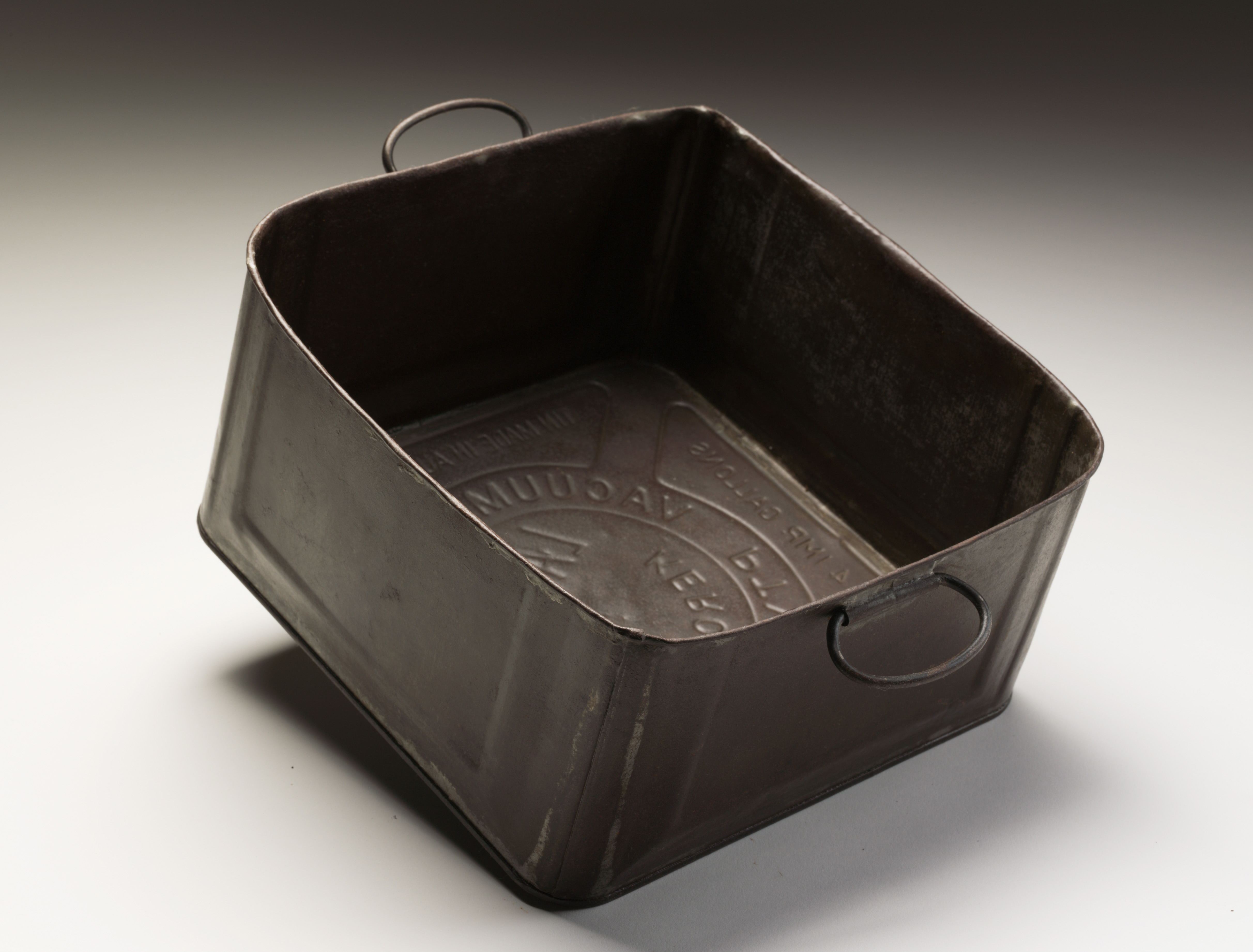  A cooking container made from a kerosene tin cut down crossways and with a round lip turned back and soldered. Two tin brackets have been soldered on opposite sides for wire handles. The container is brown and has a circular design printed in the bottom of it that reads "VACUUM OIL COMPANY PTY LTD. / LAUREL KEROSENE".